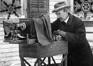 Man outside in the snow looking into old-fashioned camera apparatus.