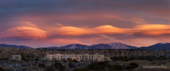 4 orange lenticular clouds in sunset light over distant mountains.