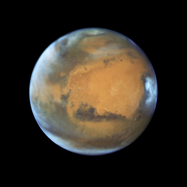 View larger. | This image shows our neighbouring planet Mars, as it was observed shortly before opposition in 2016 by the NASA/ESA Hubble Space Telescope. Some prominent features of the planet are clearly visible: the ancient and inactive shield volcano Syrtis Major; the bright and oval Hellas Planitia basin; the heavily eroded Arabia Terra in the centre of the image; the dark features of Sinus Sabaeous and Sinus Meridiani along the equator; and the small southern polar cap. Image via NASA, ESA, Hubble Heritage Team, J. Bell, M. Wolff. 