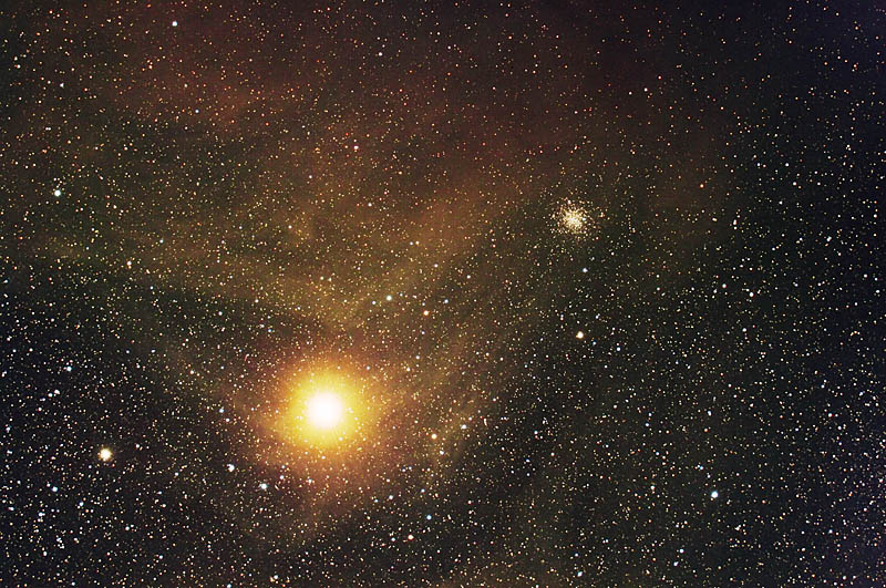 Telescopic view of Antares with nebula and nearby star cluster.