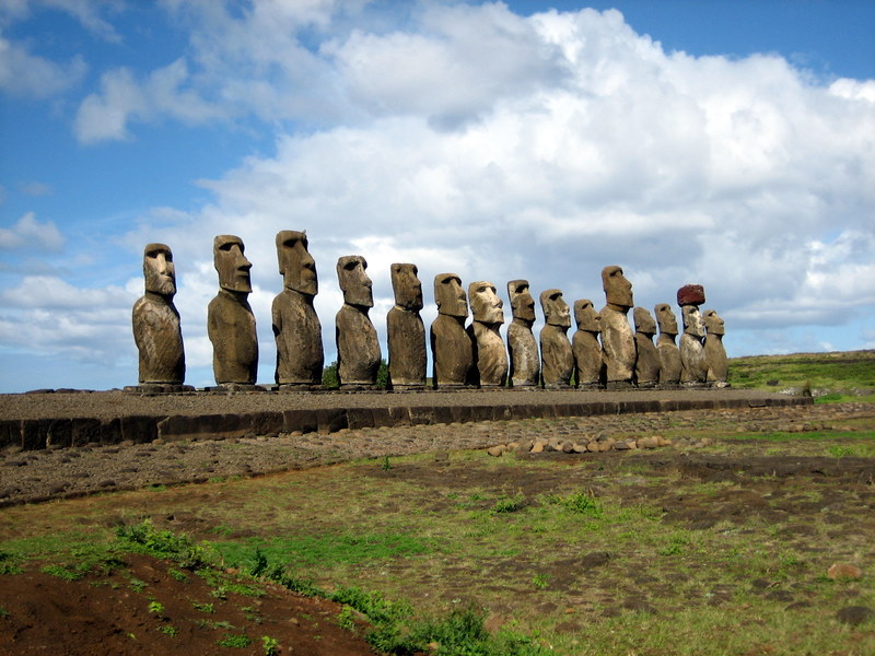 Huge monolithic stone statues on a long stone platform lined up against blue sky.