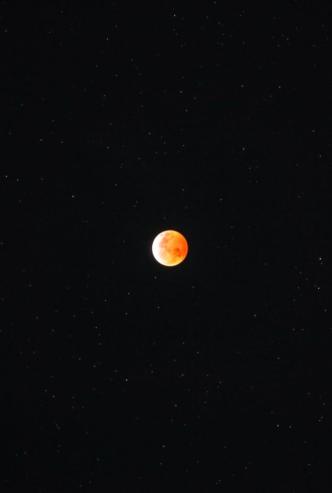 Bright orange eclipsed moon, on black background, with scattered stars.