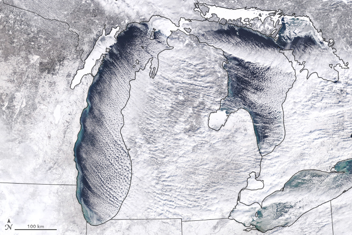 White and gray satellite view of Great Lake area, lines of clouds over lakes, land all white.