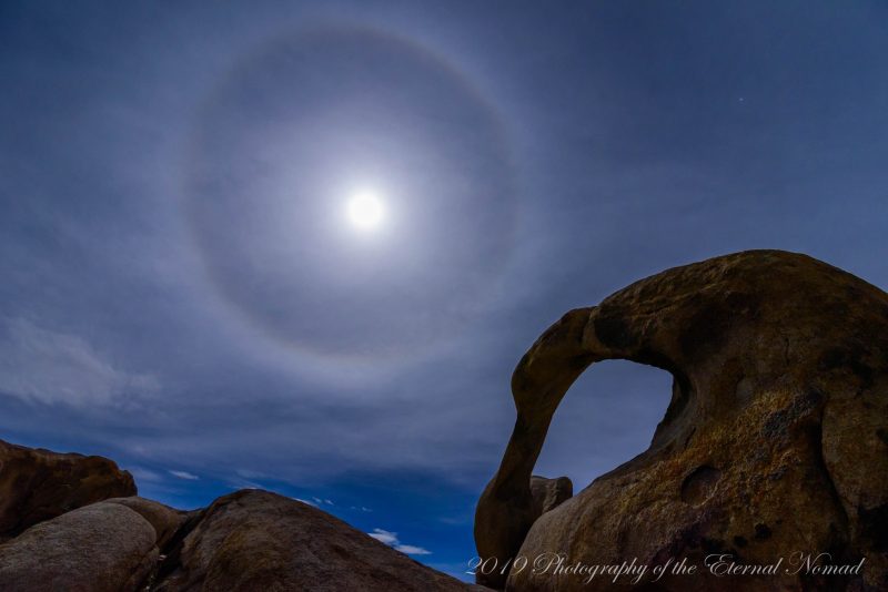 Moon with halo over twisted-looking large rock arch.