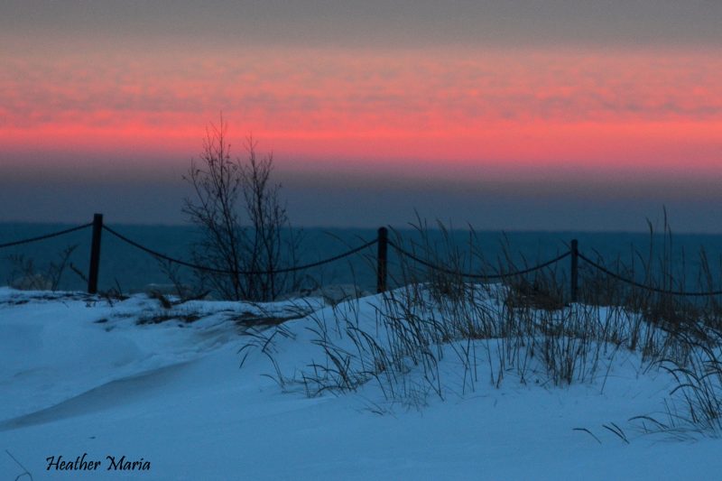 snow on dunes in foreground, ocean, pink strip of sunrise