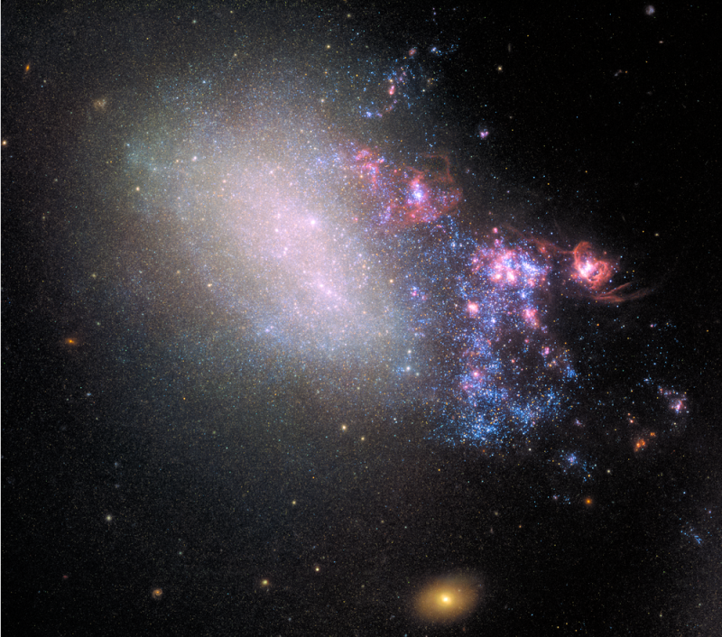 A galaxy, about a third of which is on one side, contains clusters of bright blue stars and pink nebulae.
