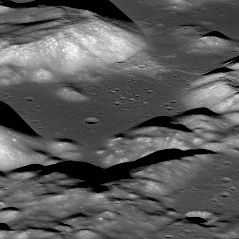 Gray and white pattern of irregular hills, with smaller black shadows and craters.