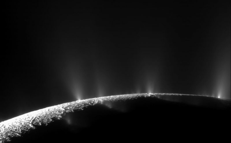 Narrow lighted crescent of Enceladus with 3 small bright vertical plumes on horizon.
