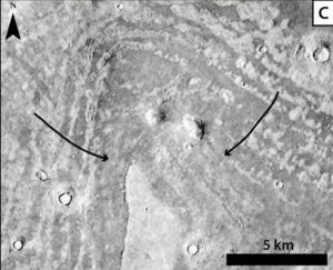 V-shaped area of concentric ridges peppered with craters and with two arrows marking locations.