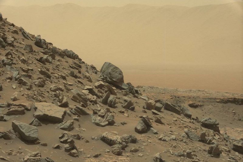 Rocks on a steep hillside on Mars under dull pink-yellow sky.