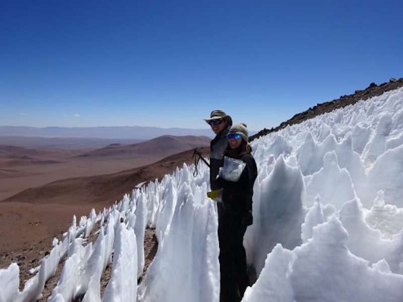 Man standing in field of waist-high pointy snow spikes on side of high mountain.