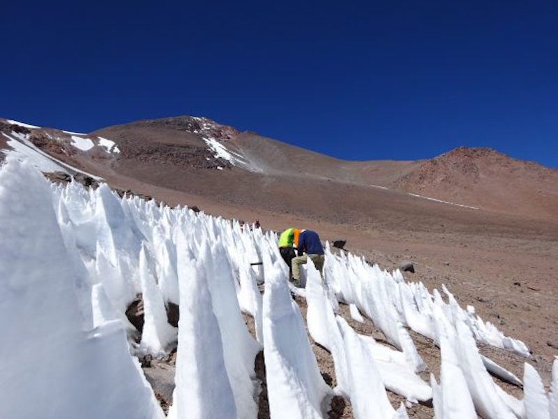 Very pointy ice cones on barren brown mountainside, cobalt blue sky.