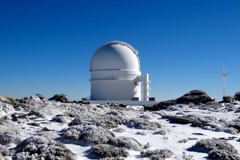 White-domed observatory on snowy, rocky mountain top.