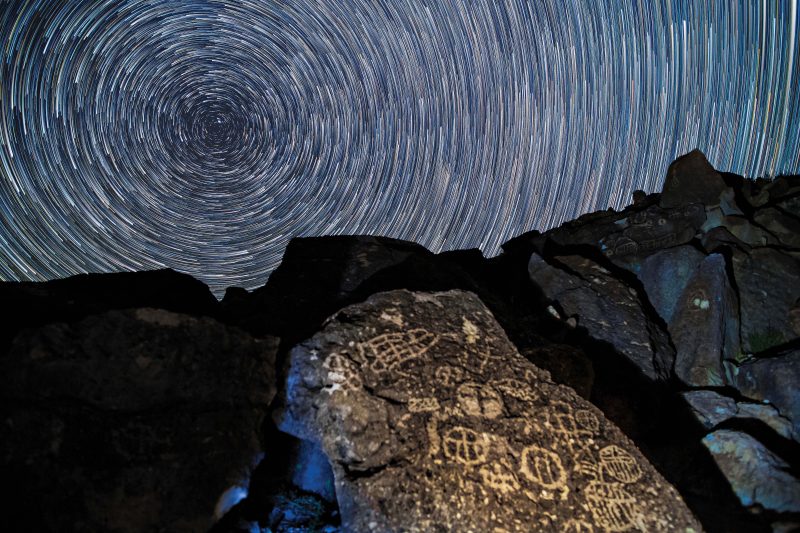 Concentric white circles filling the sky over large rock with symbols carved into it.