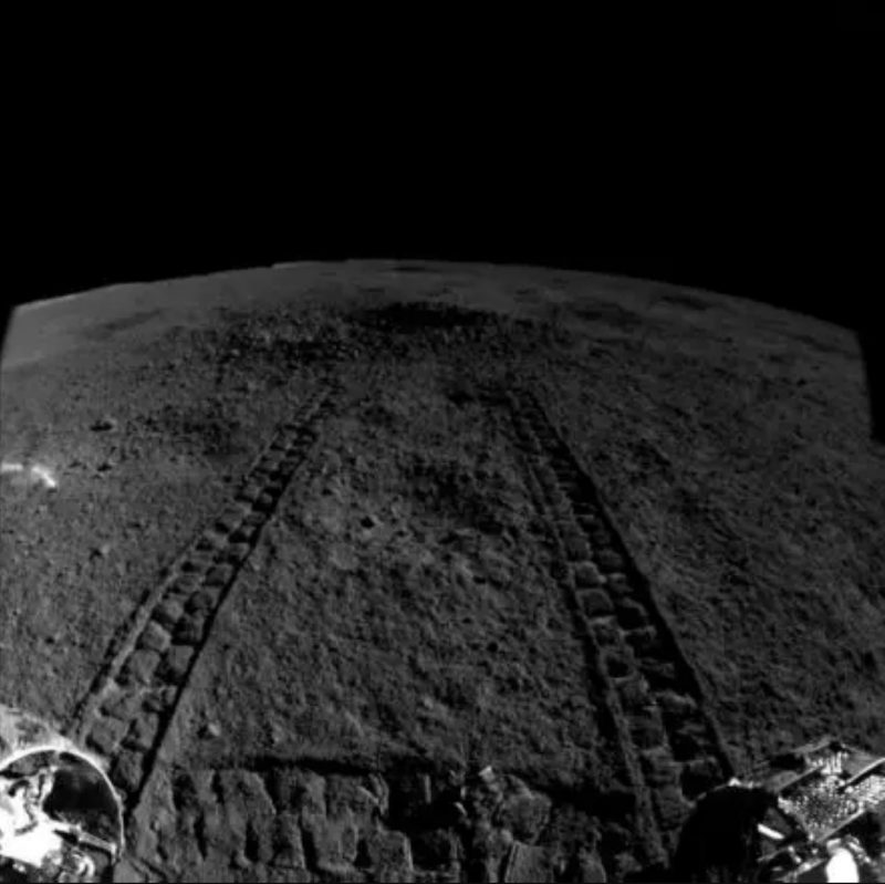 Rover tracks on rocky gray landscape with black sky.