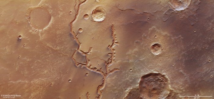Natural color satellite view of tan landscape with craters and winding, darker river.