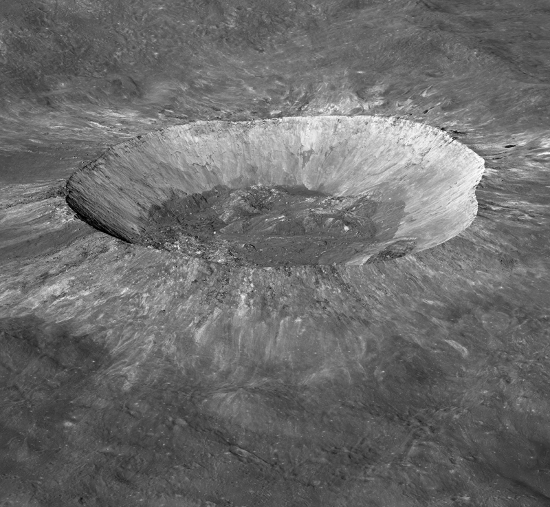 Vista oblíqua da grande cratera na lua, com lados inclinados em cinza mais claros e centro escuro.
