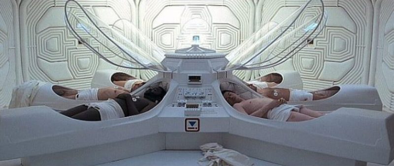 Scene from a movie, with nearly nude astronauts lying in coffin-like hibernation capsules.