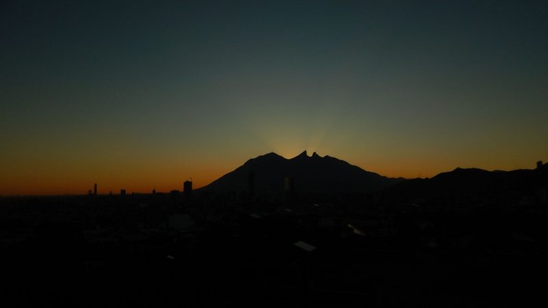 silhouette of 2 peaks with orange light behind them.