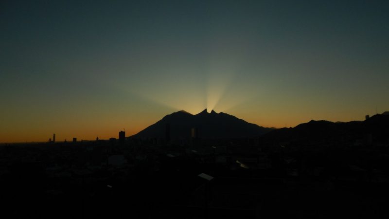 silhouette of 2 peaks with orange light behind them and sun rays between them.