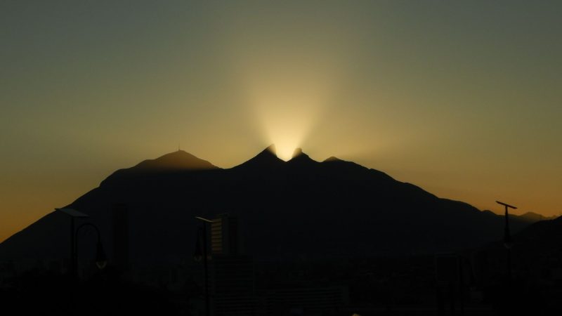 Mountain silhouette with yellow-orange light emanating between 2 peaks.