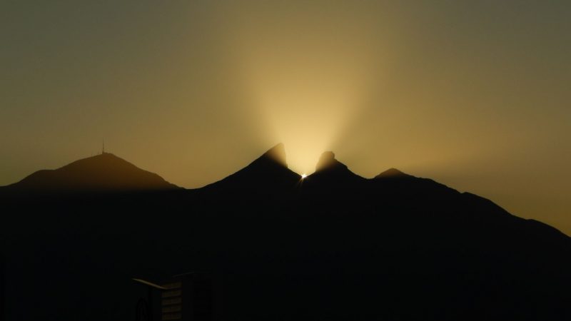 Mountain silhouette with yellow-orange light emanating between 2 peaks.