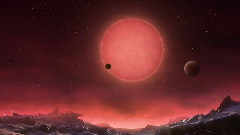 Icy landscape with red star and planets in sky.